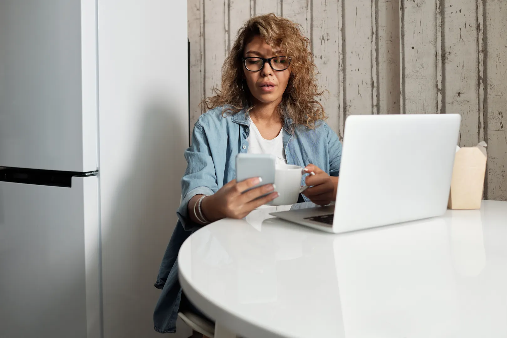 A woman engages in remote work, using a smartphone and laptop at home.