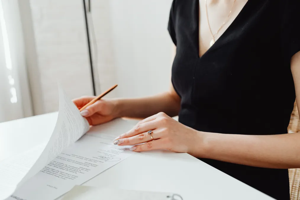 A faceless person reads a multi-page contract at a desk