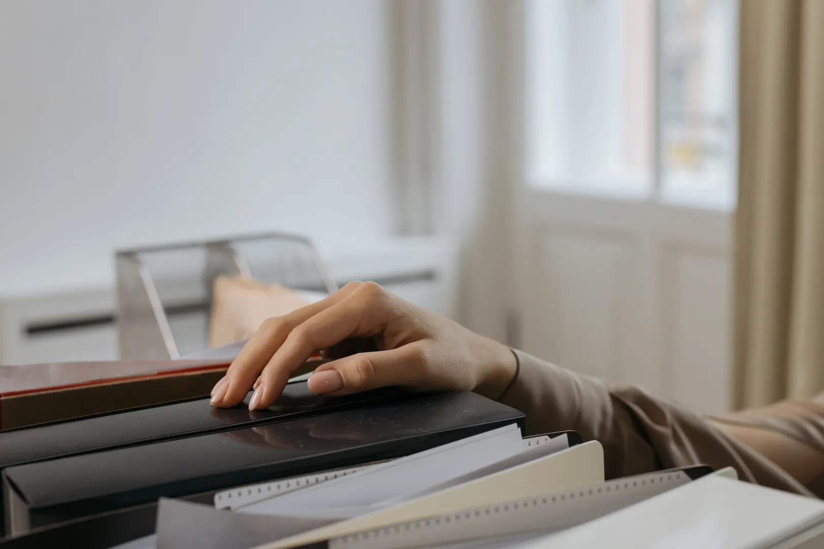 An adult's hand reaches for office file folders, capturing a thoughtful moment. Indoors setting.