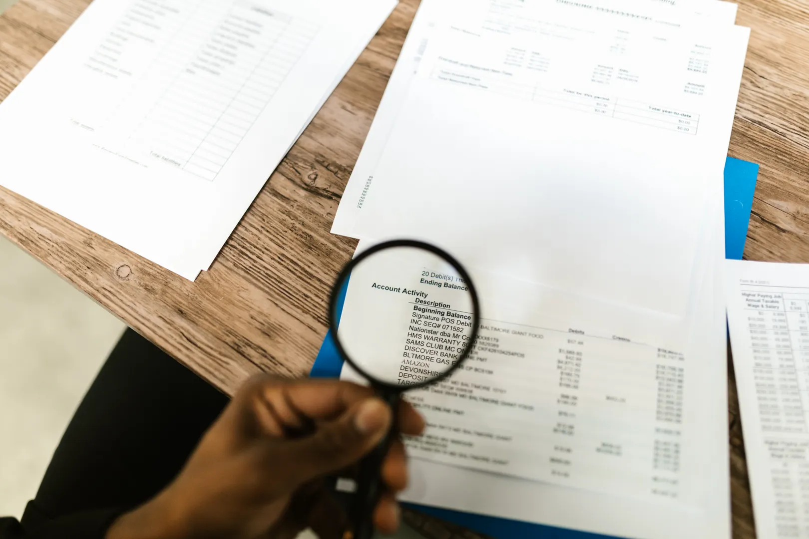 A hand uses a magnifying glass to inspect a financial statement