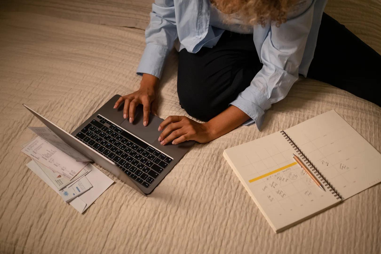 A person works on a laptop among notebooks and planning papers