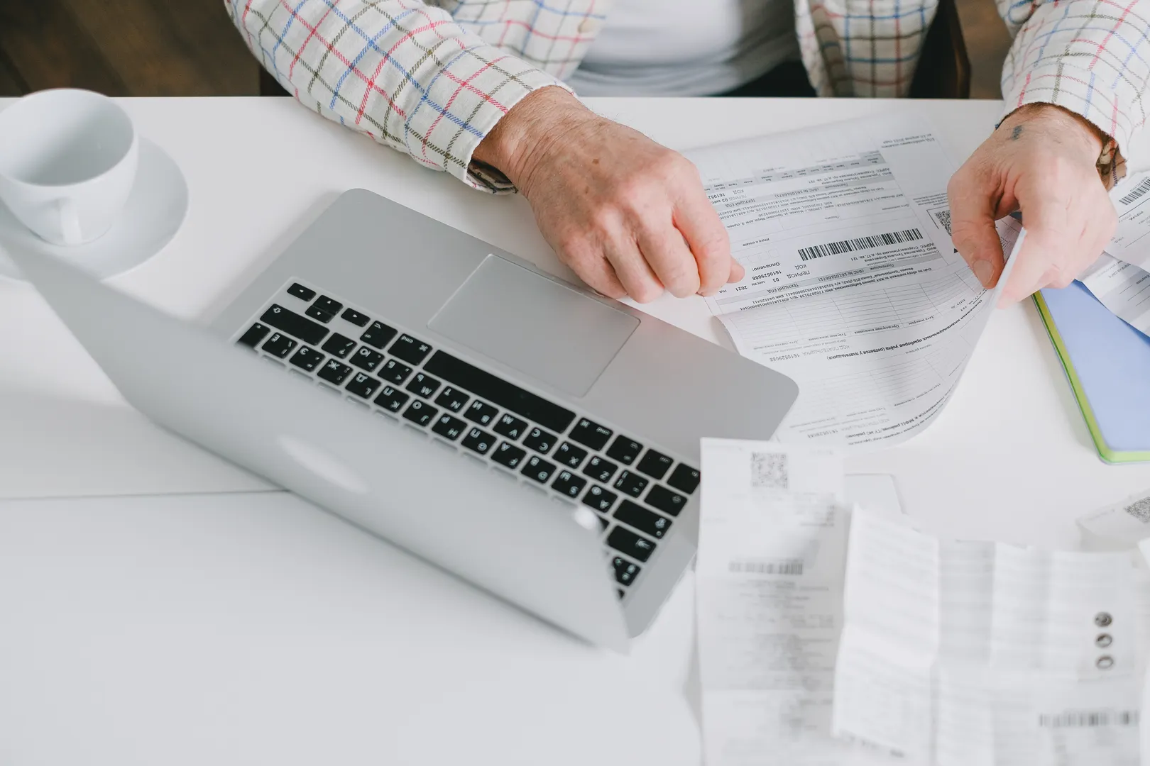 Hands compare printed paperwork beside an open laptop