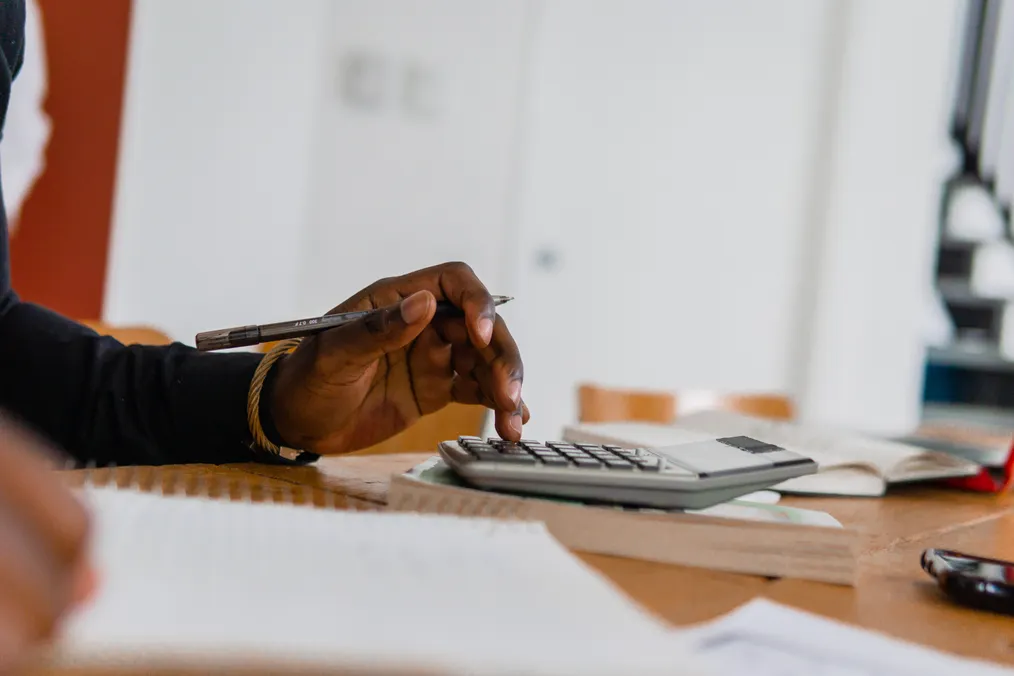 A hand uses a calculator beside budget paperwork at a table