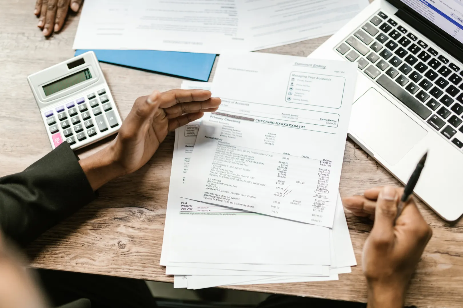 Hands review financial statements beside a calculator and laptop