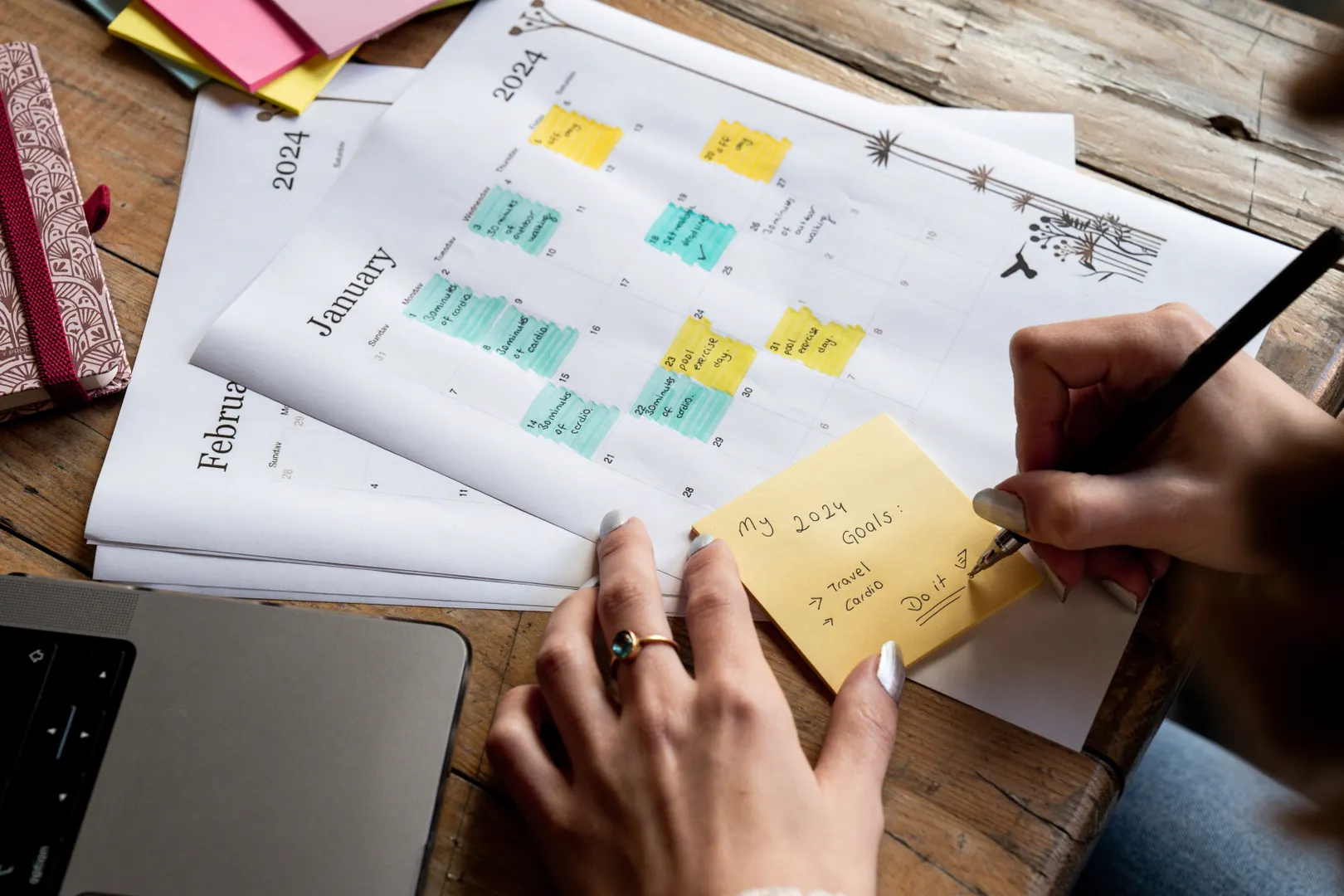 Hands marking dates and sticky notes on a monthly planner