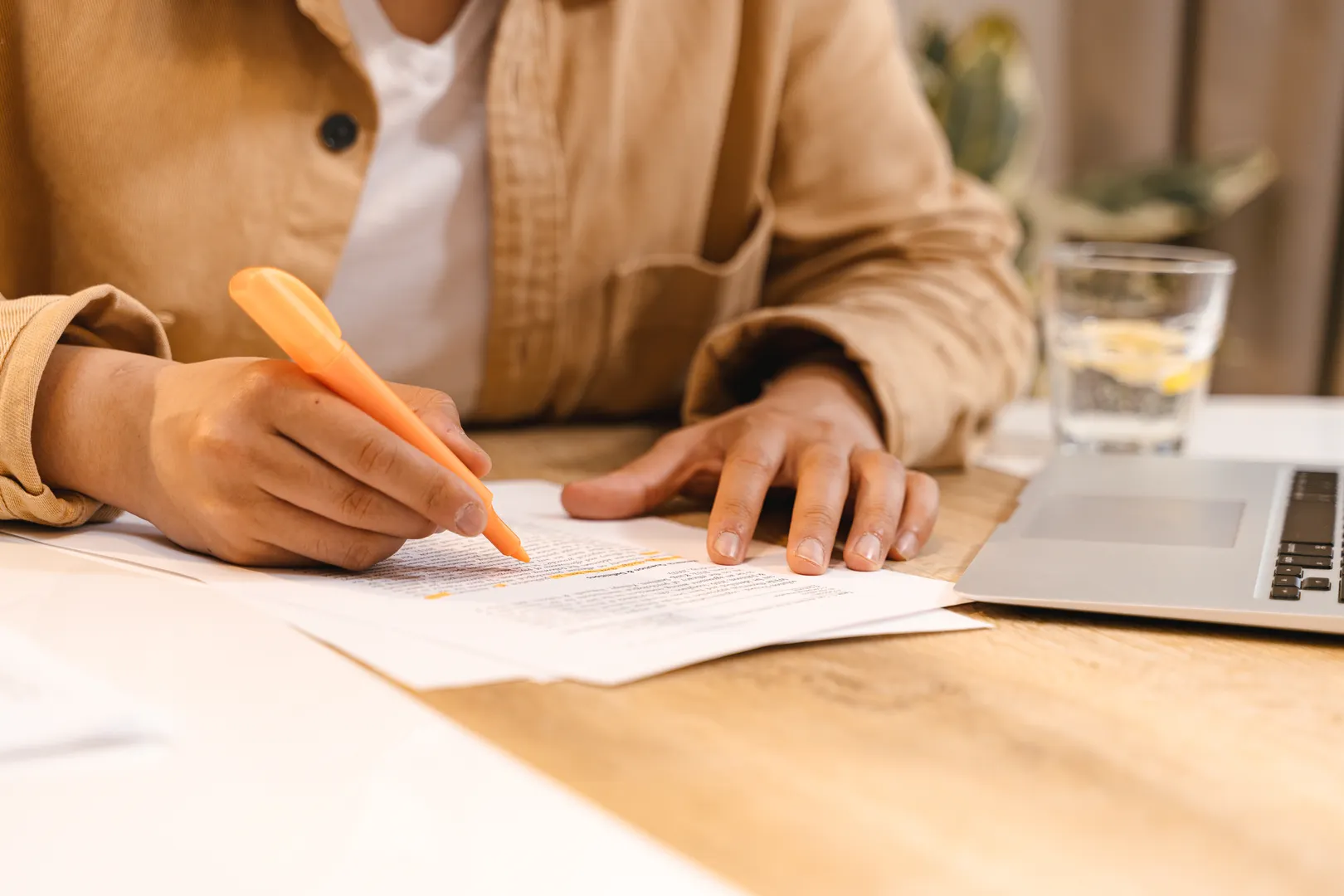 Person highlighting paperwork beside an open laptop