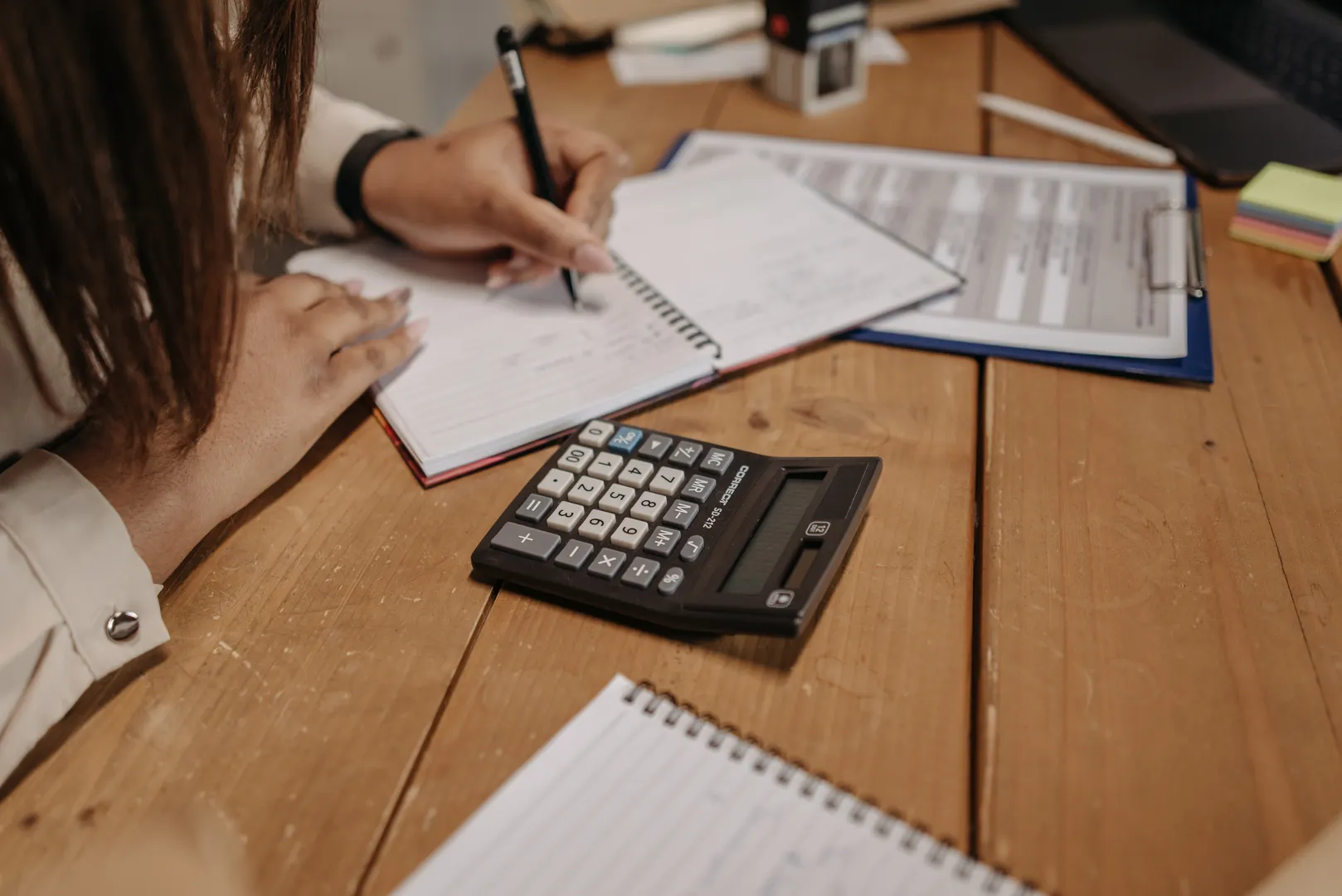 Person writing notes beside paperwork and a calculator