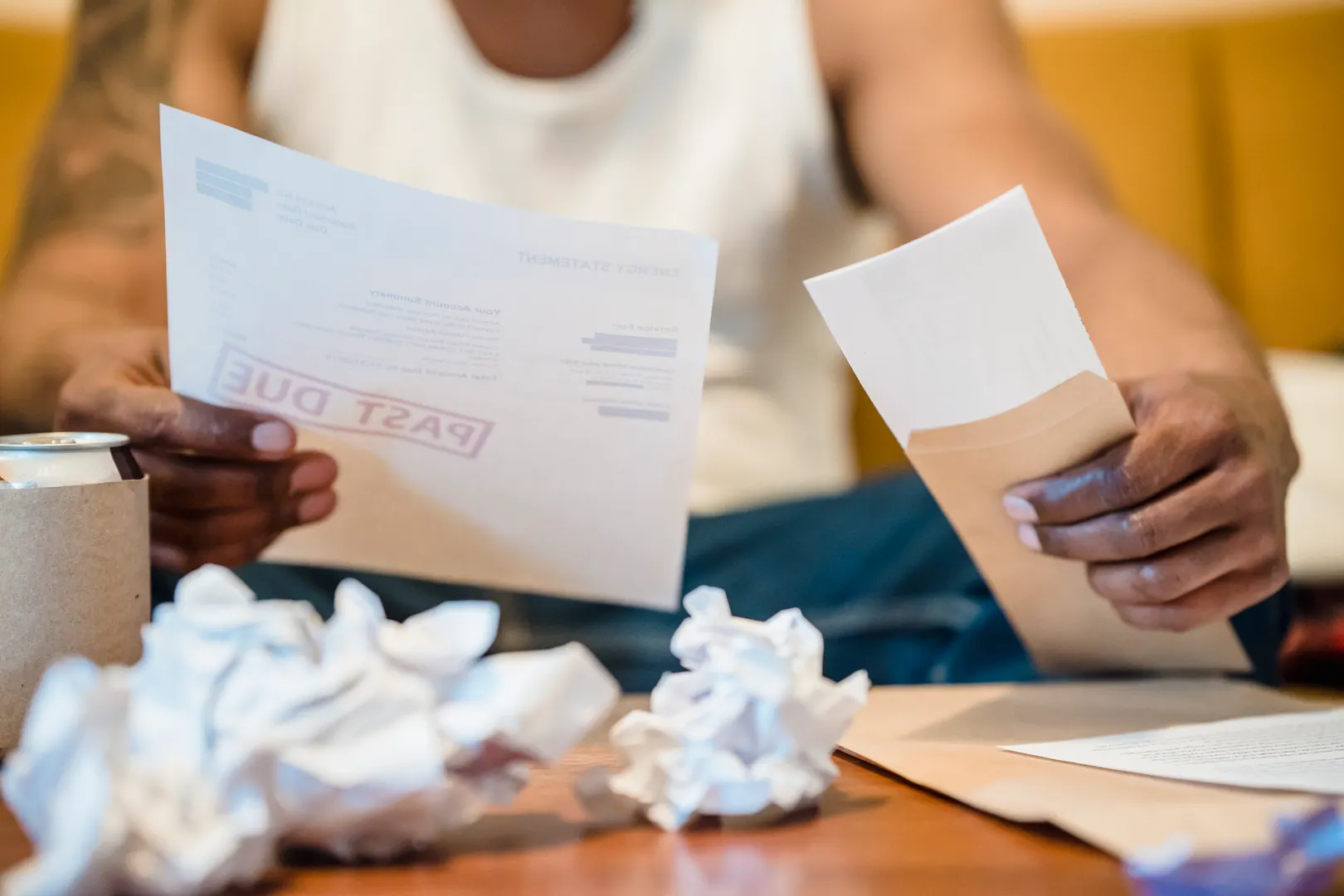 Man reviewing a stamped past-due bill and envelope amid crumpled papers on a table