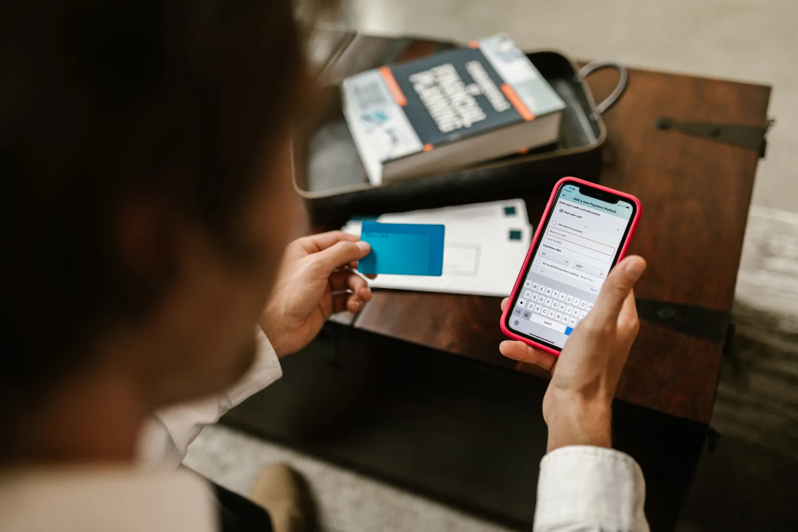 Hands holding a phone and a card over paperwork and a book on a desk