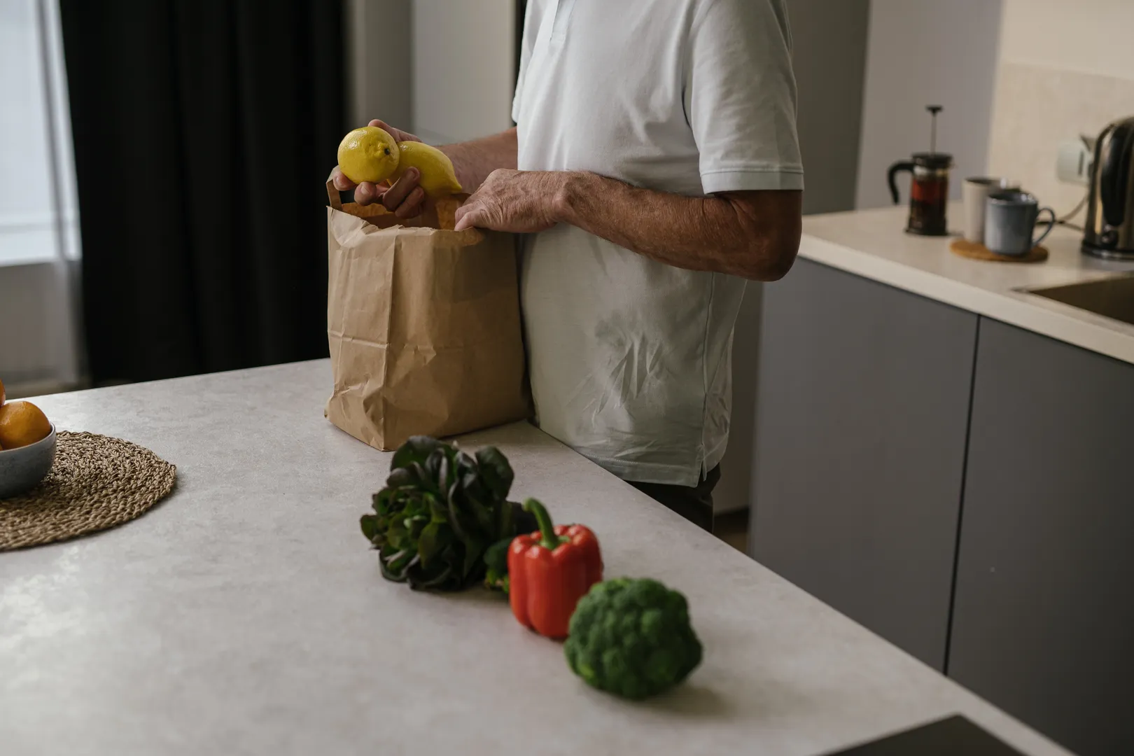 A person unpacking fresh fruit and vegetables onto a kitchen bench