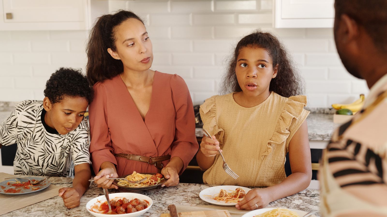 A mother and her children sharing a home-cooked pasta meal at the kitchen counter