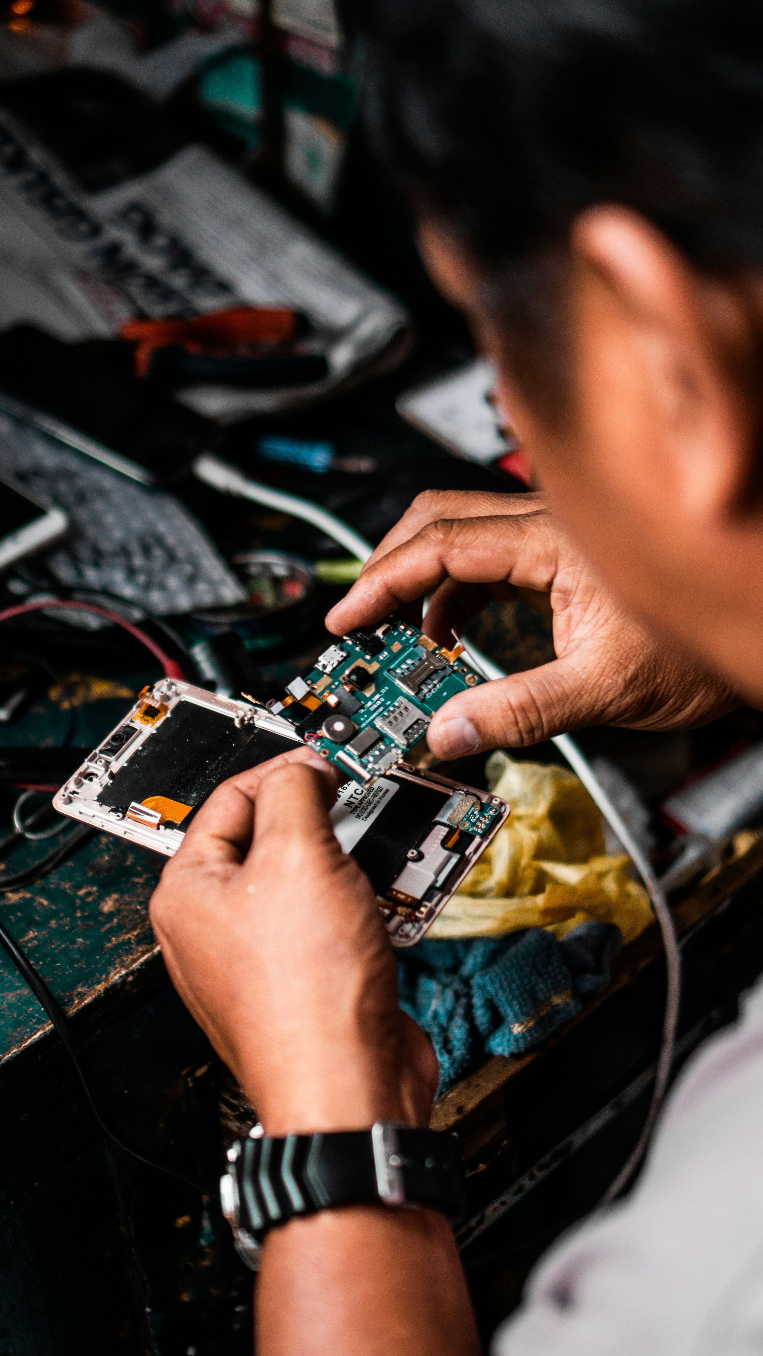 Hands working on the internal components of a phone at a repair bench