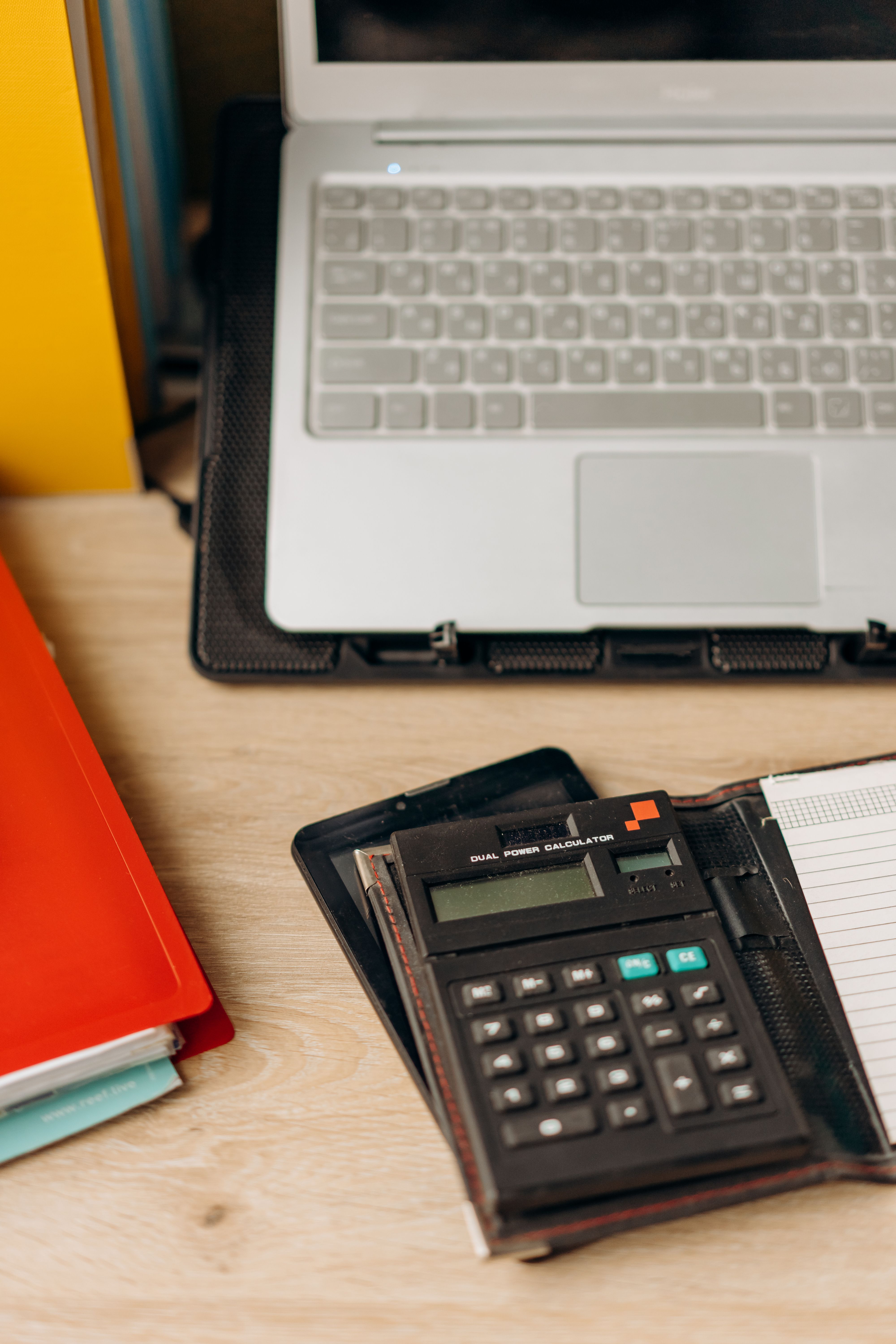 A laptop, calculator and notebooks on a wooden desk