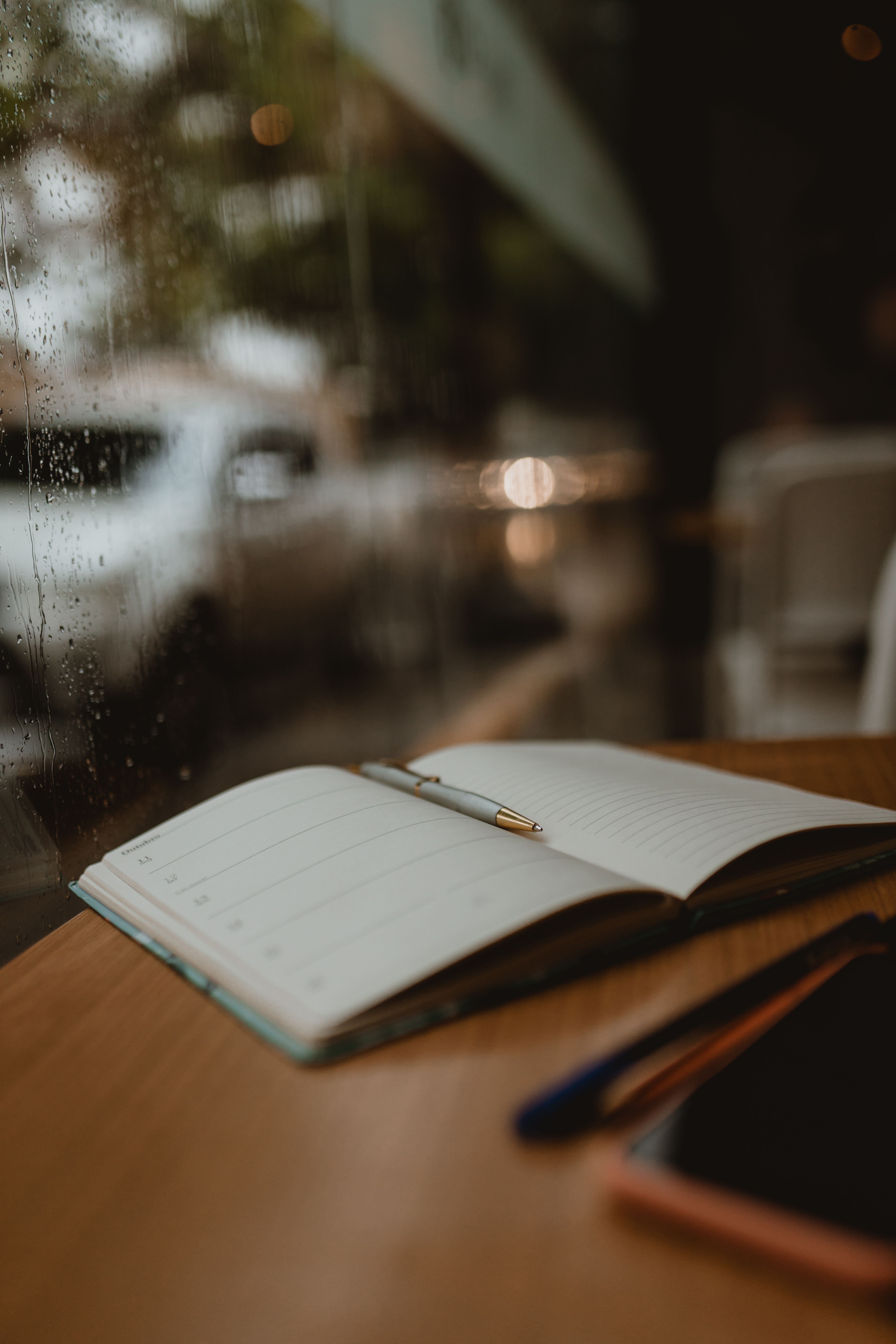 An open notebook and pen beside a rain-covered window