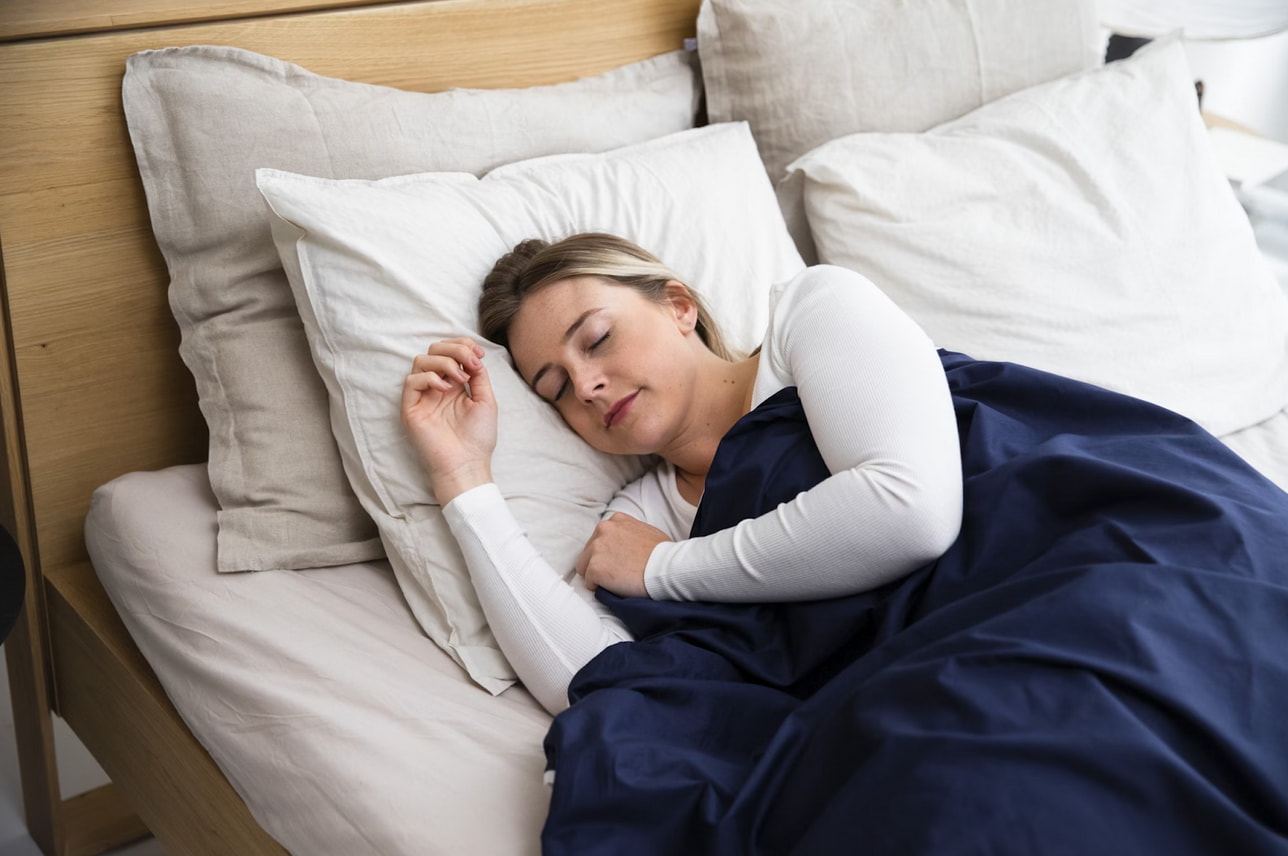 A woman peacefully sleeping in bed, covered by a soft blue blanket.