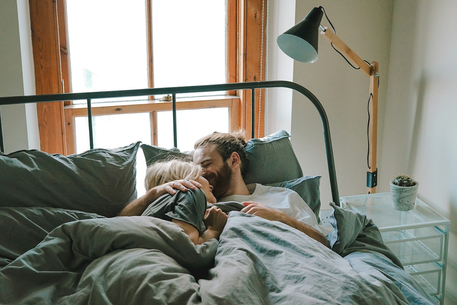 A couple lying in bed, sharing a moment of intimacy and comfort under soft blankets.