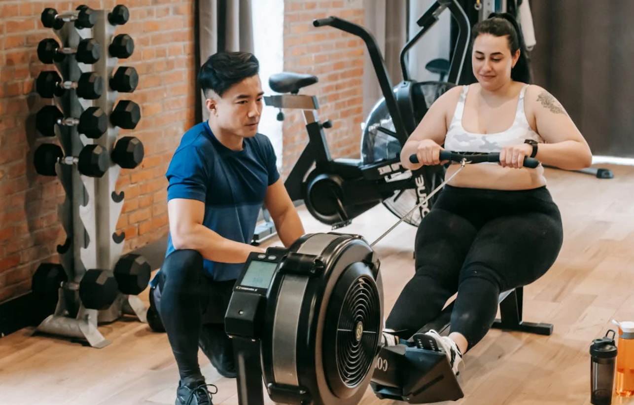 A man and woman are exercising together in a gym, using weights and engaging in a fitness routine.  