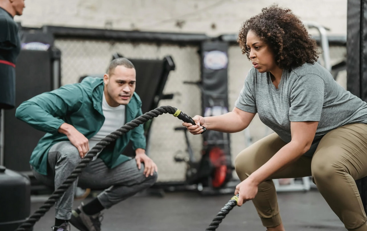 A man and woman are exercising together, using a battle rope in a gym setting. 