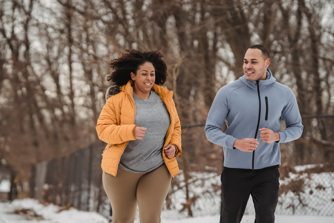 A man and woman jogging together in a snowy landscape, wearing winter athletic gear. 