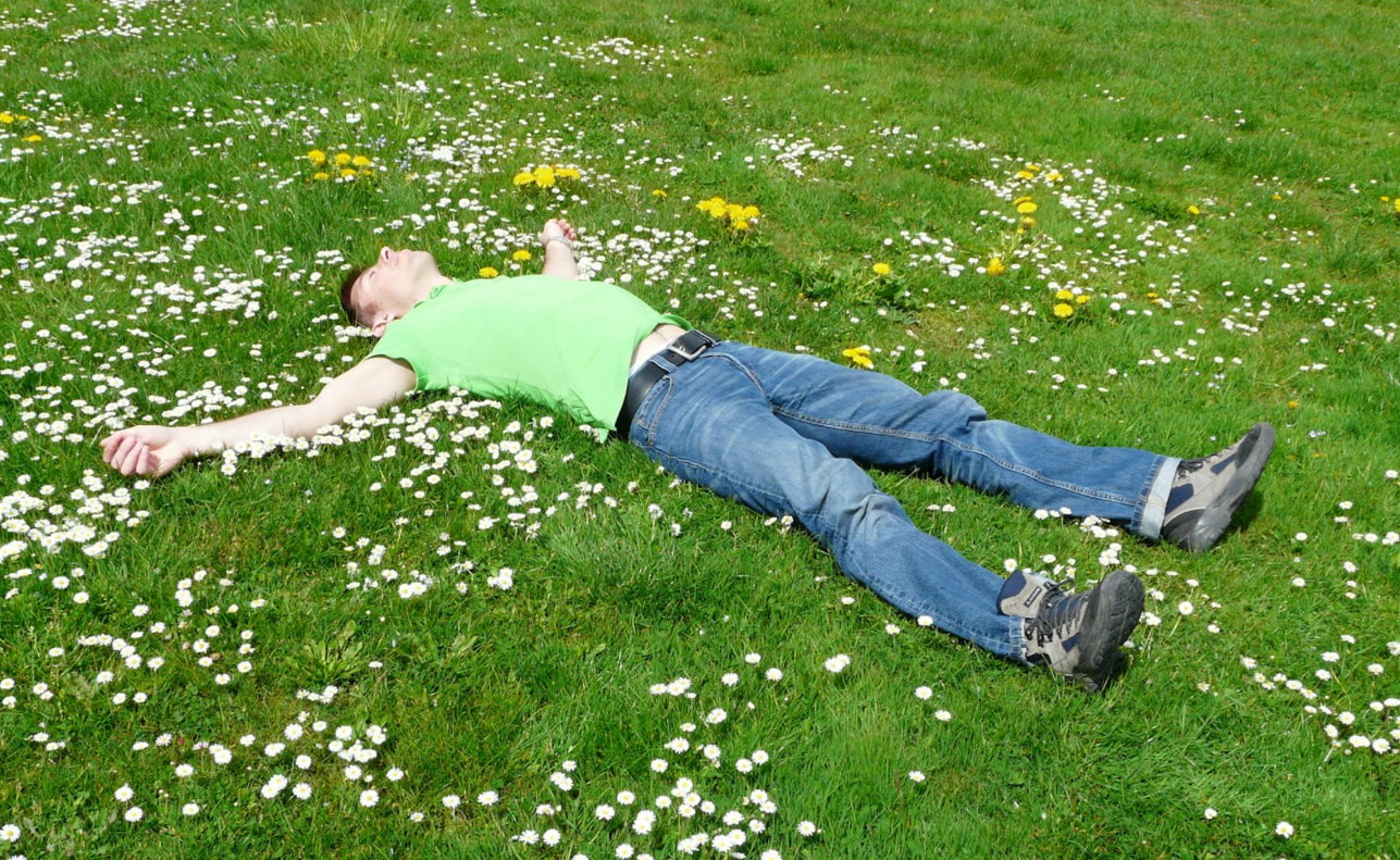 A man lies on the grass with his arms outstretched, enjoying a sunny day in a peaceful outdoor setting.  