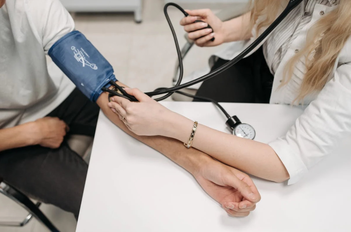 A doctor measures a patient's blood pressure using a sphygmomanometer in a clinical setting.  