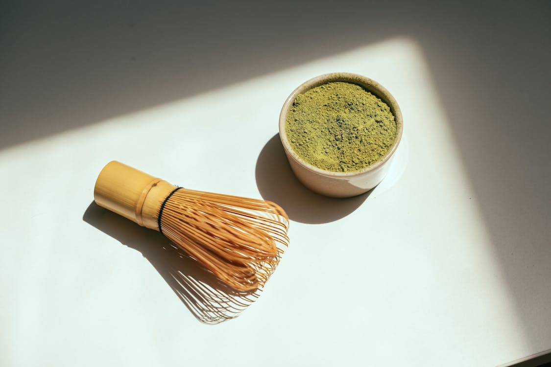 Matcha green tea powder in a bowl with a bamboo whisk beside it, ready for preparation.  