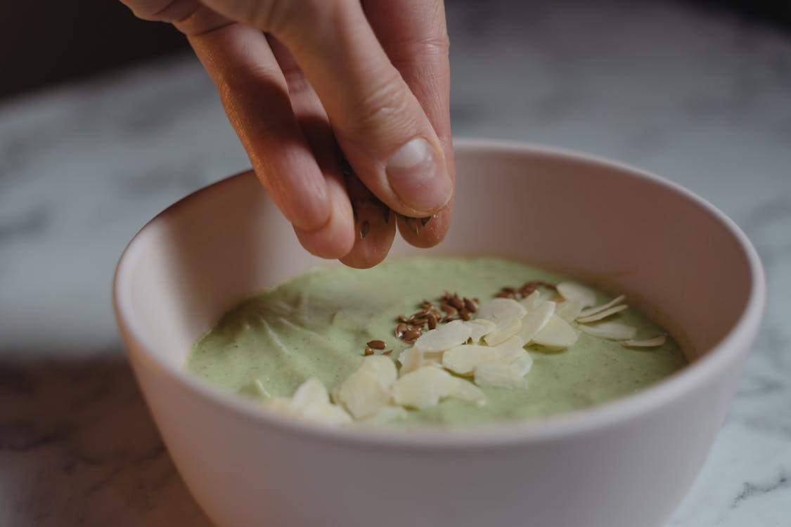 A person dips a spoon into a bowl filled with a vibrant green smoothie.