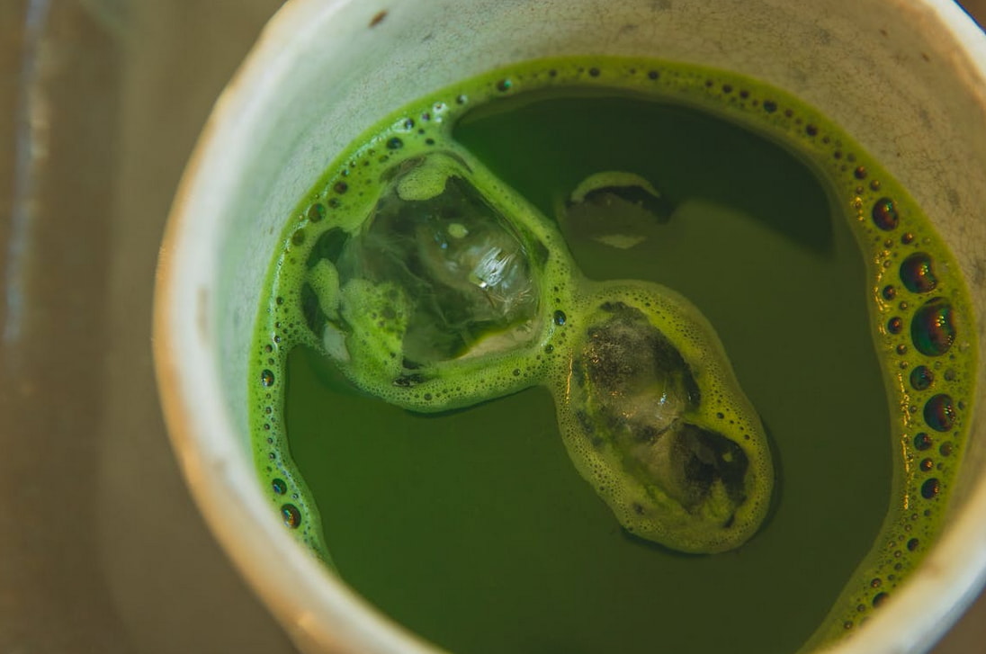 A detailed close-up of a cup of green tea, highlighting its rich green hue and the gentle steam rising from the surface.