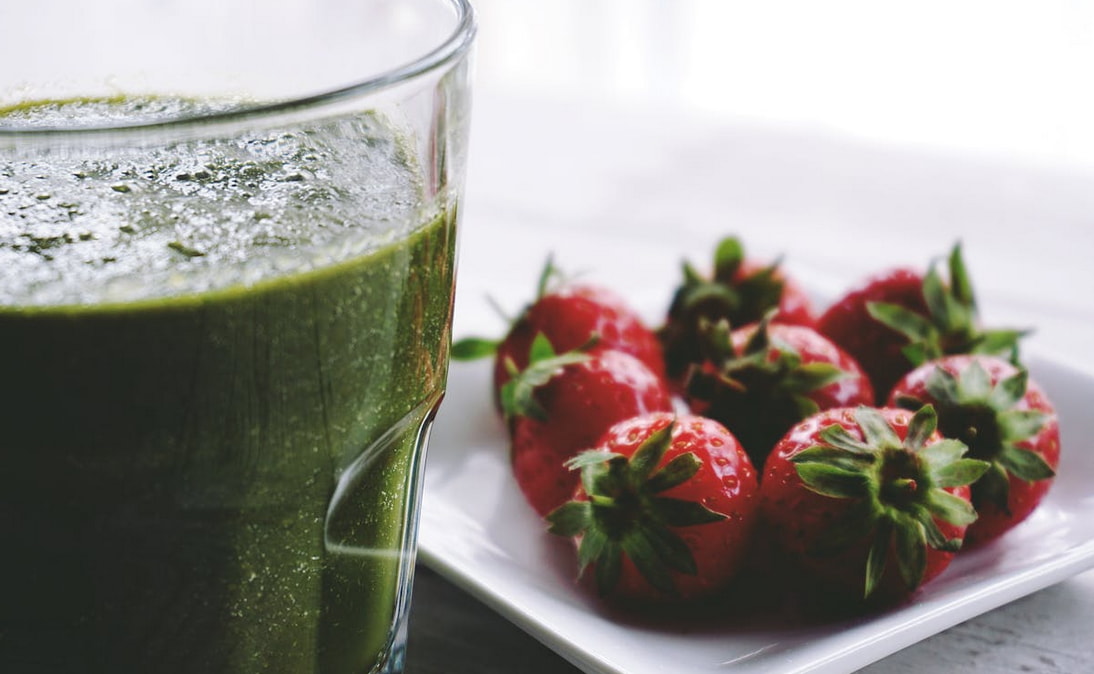 A refreshing green smoothie in a glass with strawberries arranged on a plate.