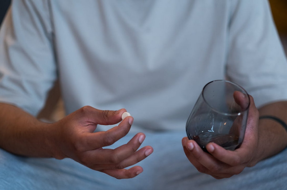 A man holds a glass of water in one hand and a pill in the other, preparing to take his medication.