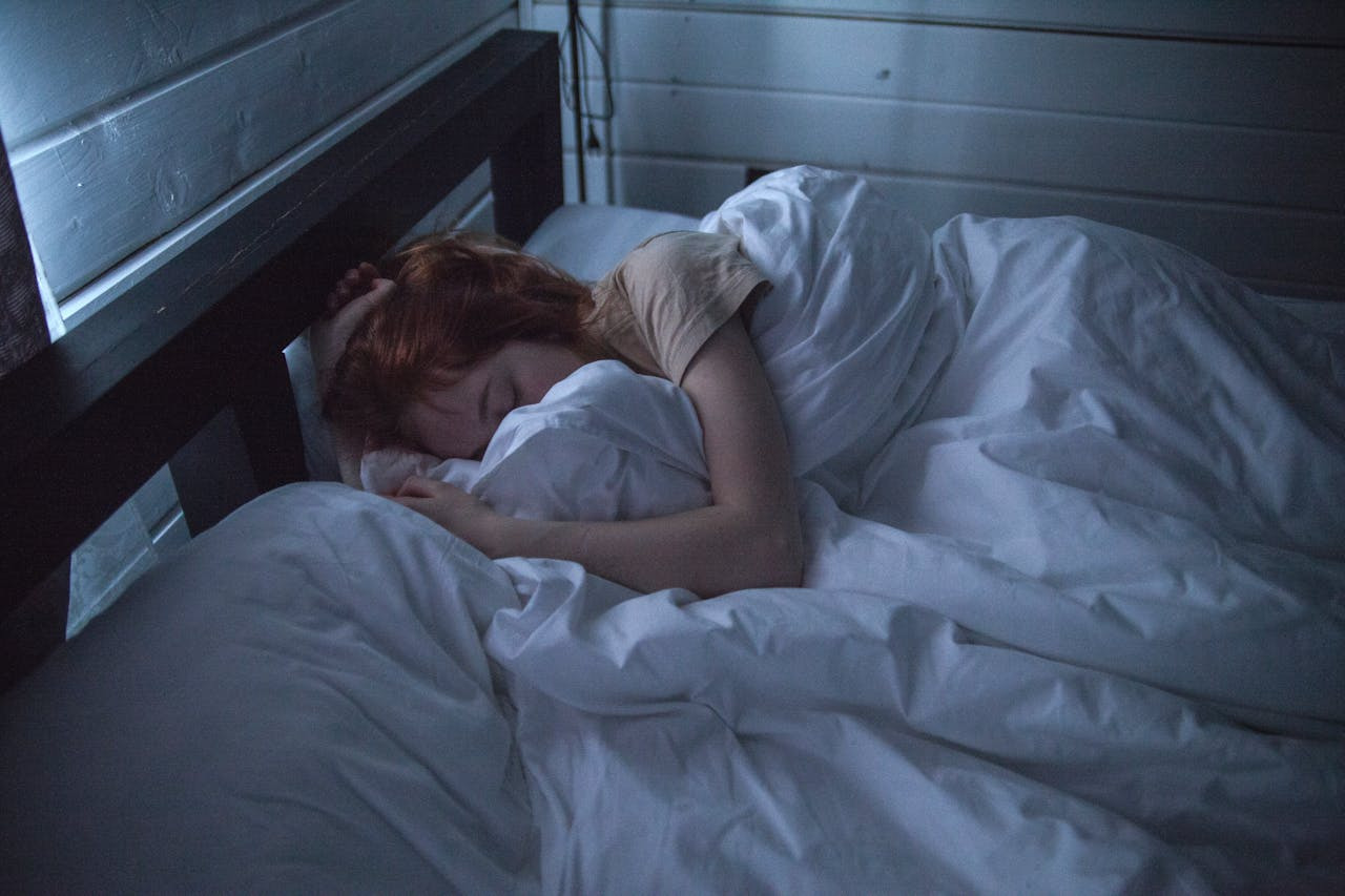 A woman peacefully sleeping in a bed adorned with white sheets.  