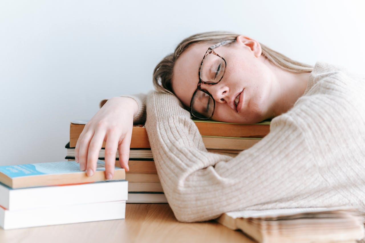 A woman peacefully sleeps atop a tall stack of books, surrounded by a cozy atmosphere of knowledge and rest.