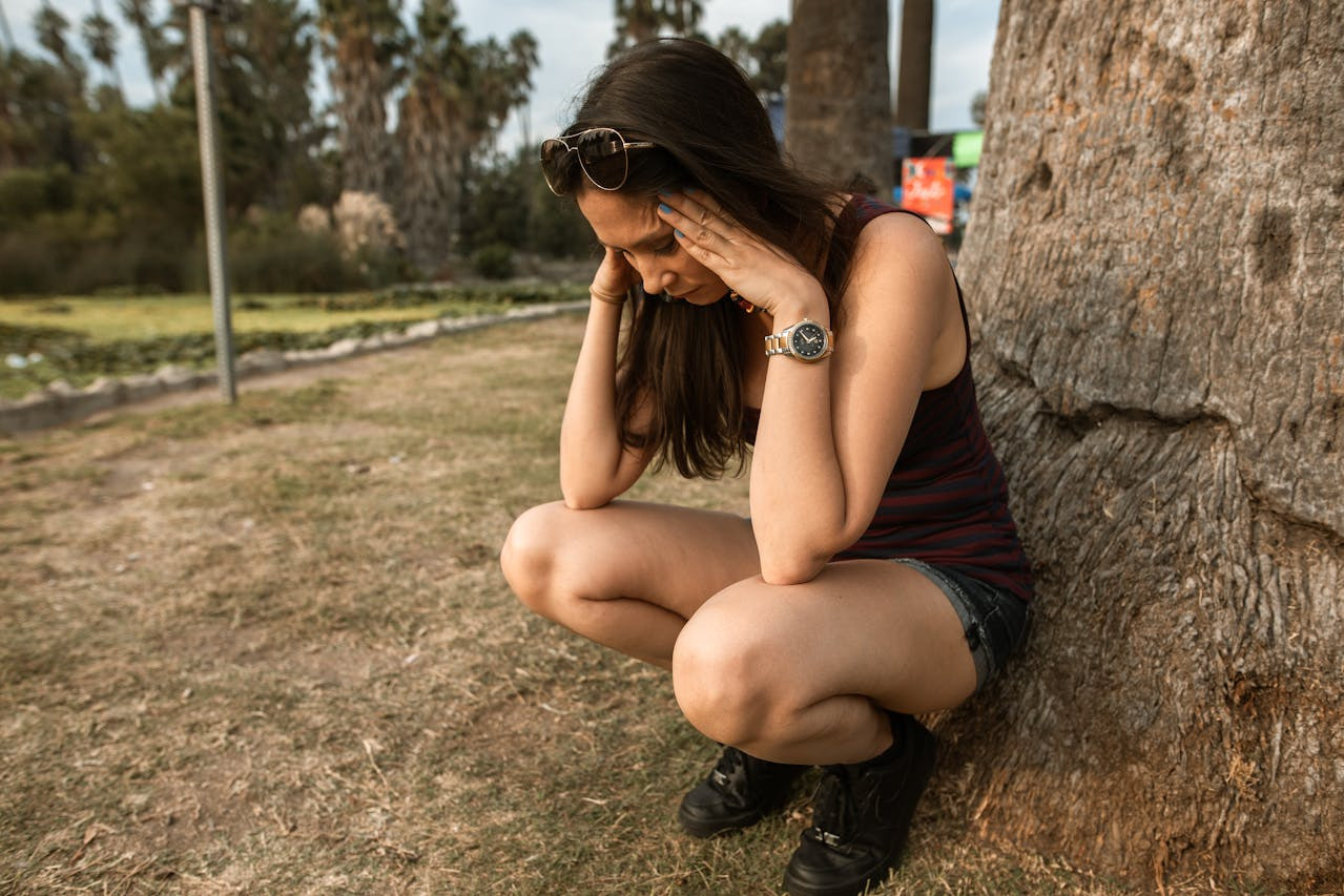 A woman sitting on the ground, her head in her hands, conveying a sense of distress or deep contemplation.  
