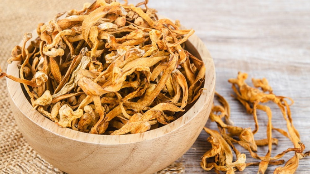 Dried yellow dock leaves arranged in a wooden bowl on a rustic wooden surface. 