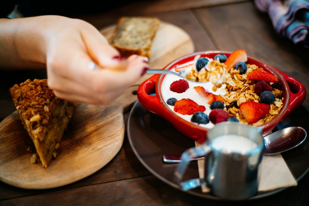 A person enjoying a bowl of cereal topped with fresh fruit and yogurt, seated at a table. 