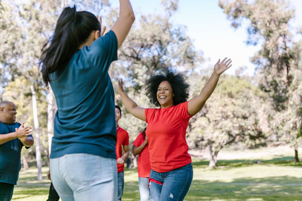 A diverse group of people in a park joyfully raising their arms, celebrating together under a clear blue sky.