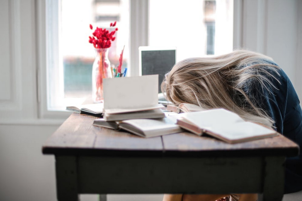 A woman sits at a desk with her head down, appearing deep in thought or concentration. 