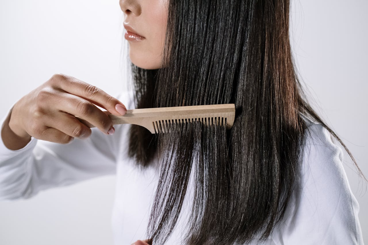 A woman is gently combing her long hair with a comb, focusing on smoothing and styling her locks.