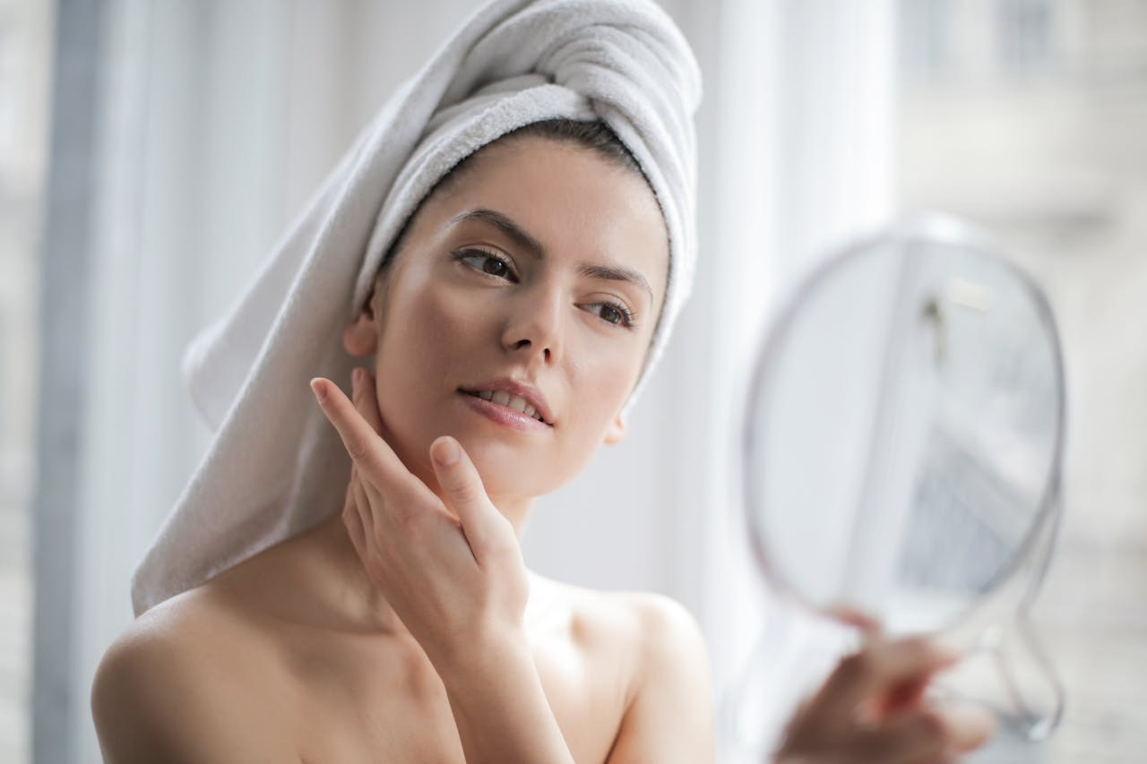 A woman gazes into a mirror while drying her hair with a towel, reflecting a moment of personal care.