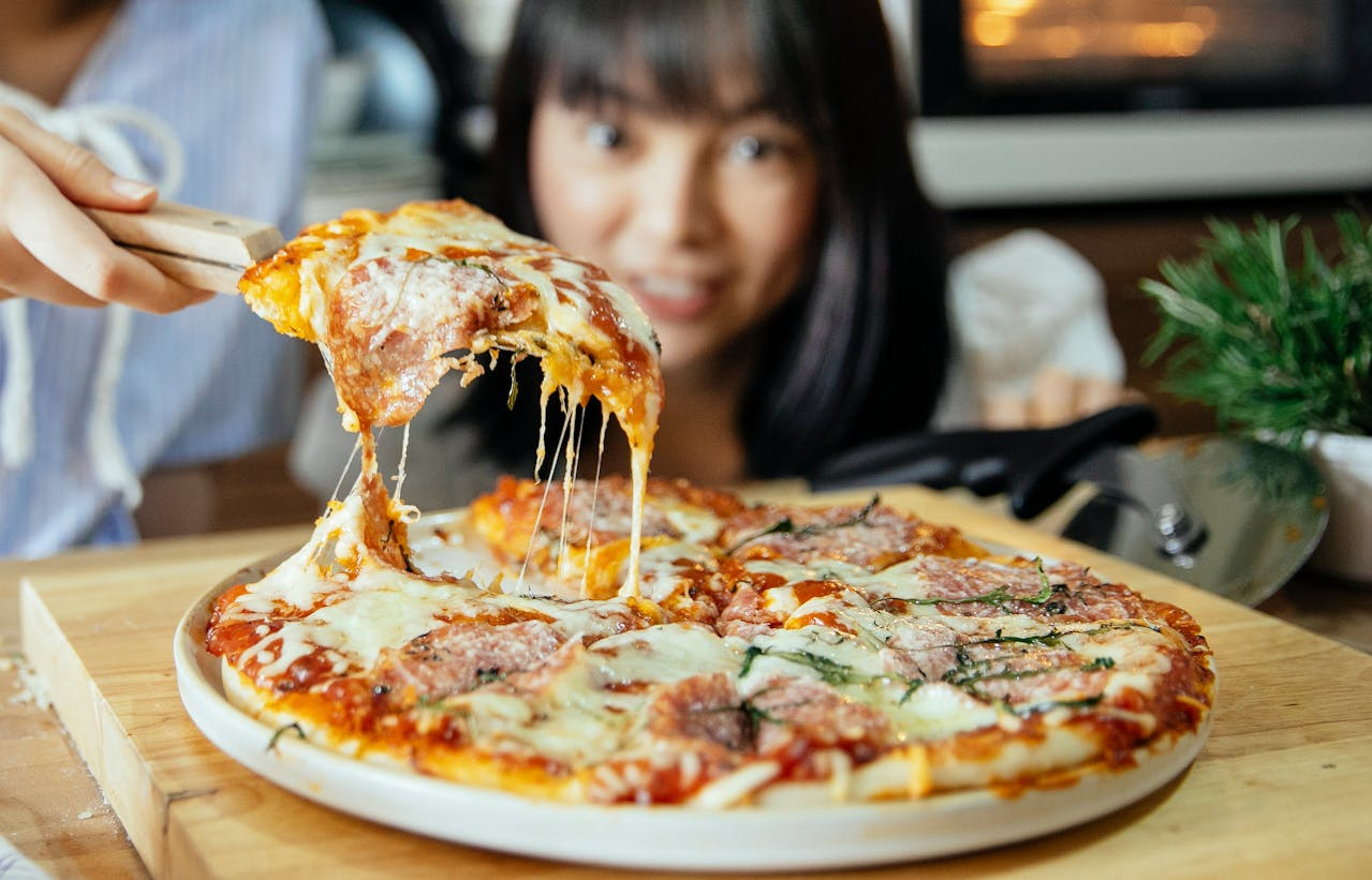 A woman is holding a slice of pizza topped with melted cheese, looking pleased and ready to enjoy it.