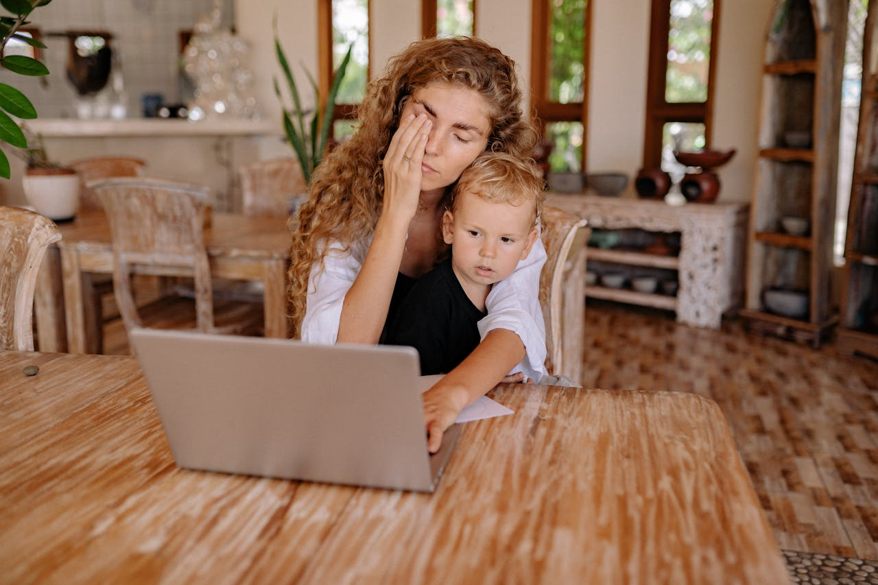 A woman and a child are seated at a table, focused on a laptop in front of them. 