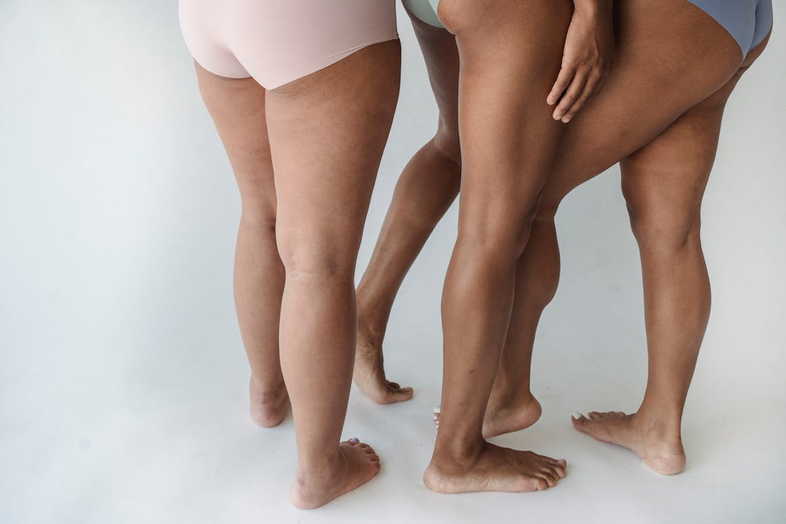 Three women in underwear standing side by side, smiling and posing for the camera in a bright, neutral setting.  