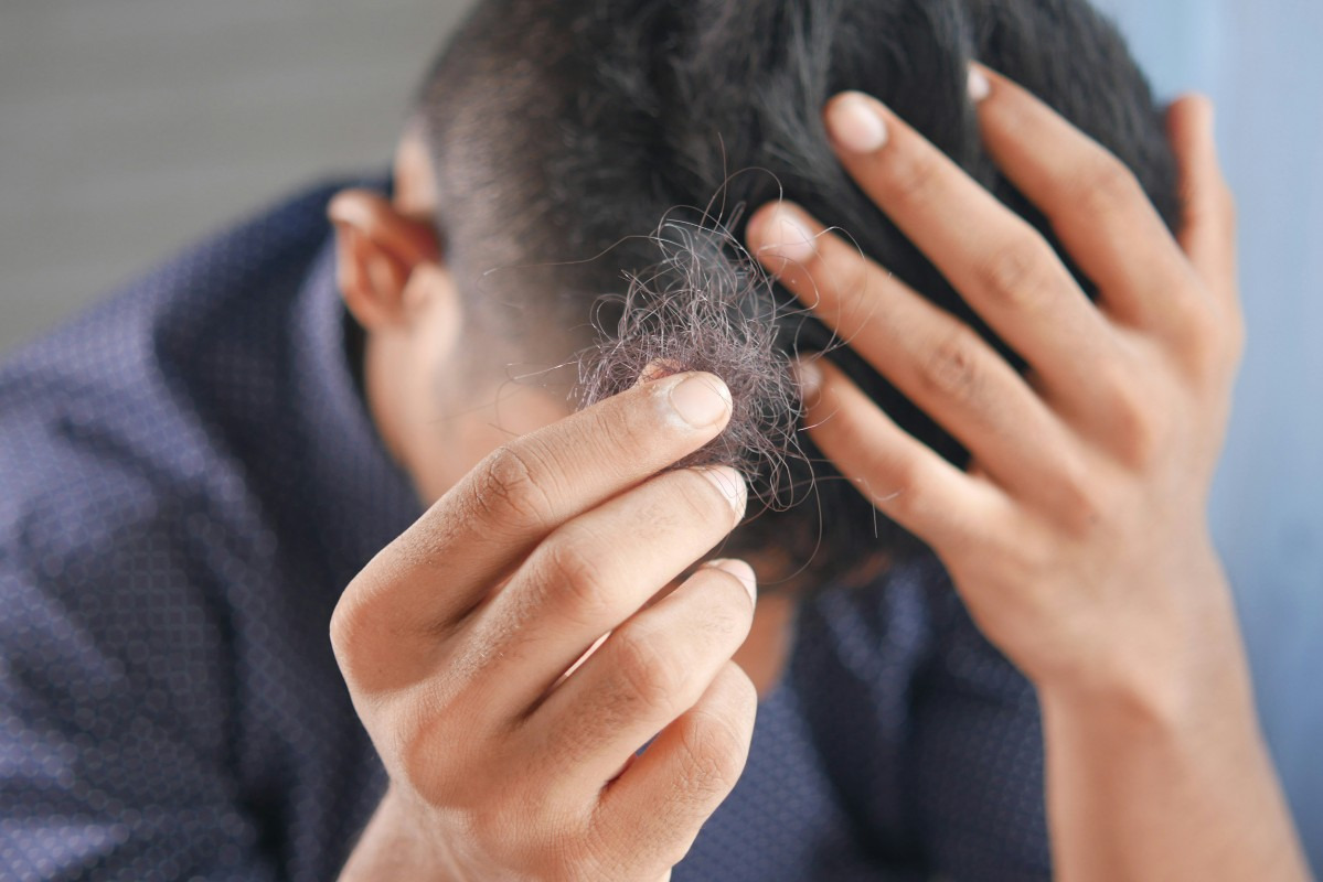 A man is using a comb to style his hair, focusing on achieving a neat appearance.  