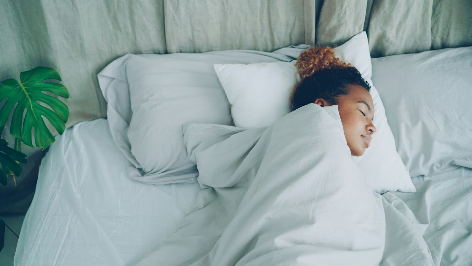 A woman resting in bed, wrapped in a cozy white blanket, with a serene expression. 