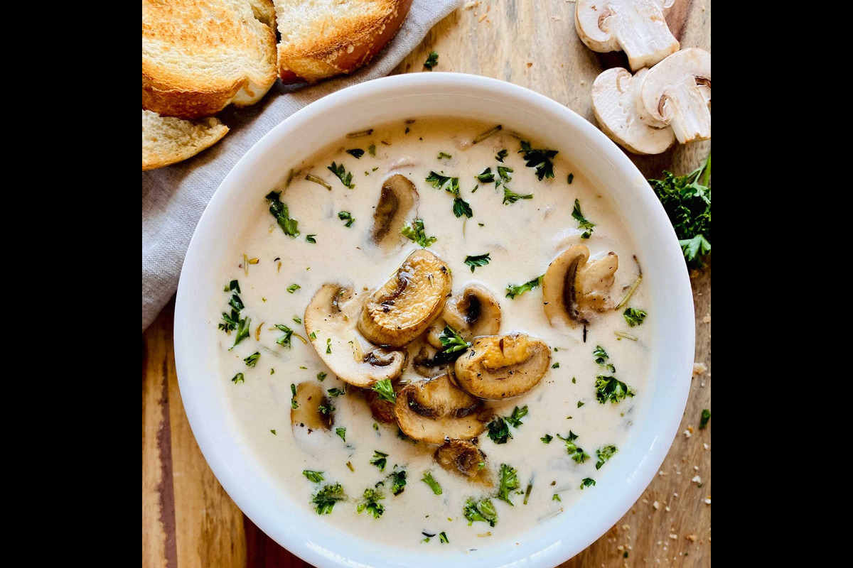 A bowl of mushroom soup accompanied by a slice of bread, showcasing a warm and inviting meal.  
