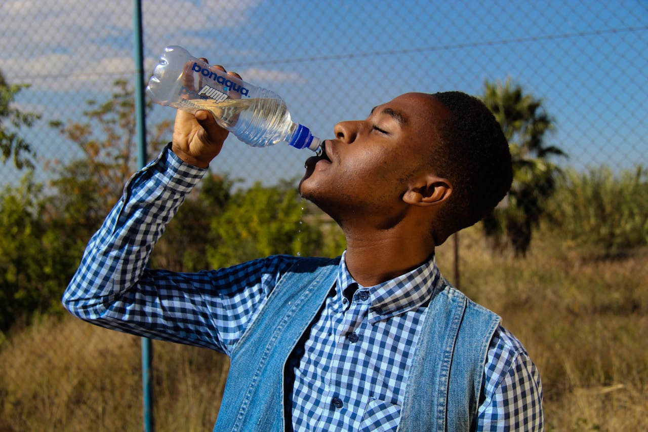 A young man takes a sip of water from a clear plastic bottle, looking refreshed and hydrated.  