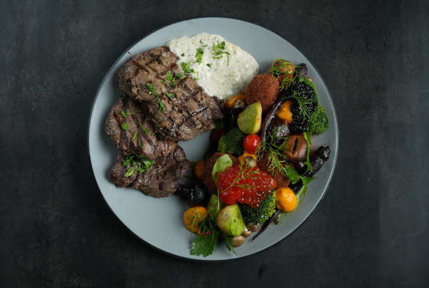 A plate featuring grilled steak accompanied by sautéed vegetables and a serving of rice.