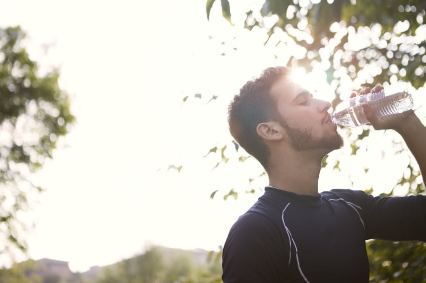 A man is seen drinking from a water bottle, staying hydrated in a warm environment.