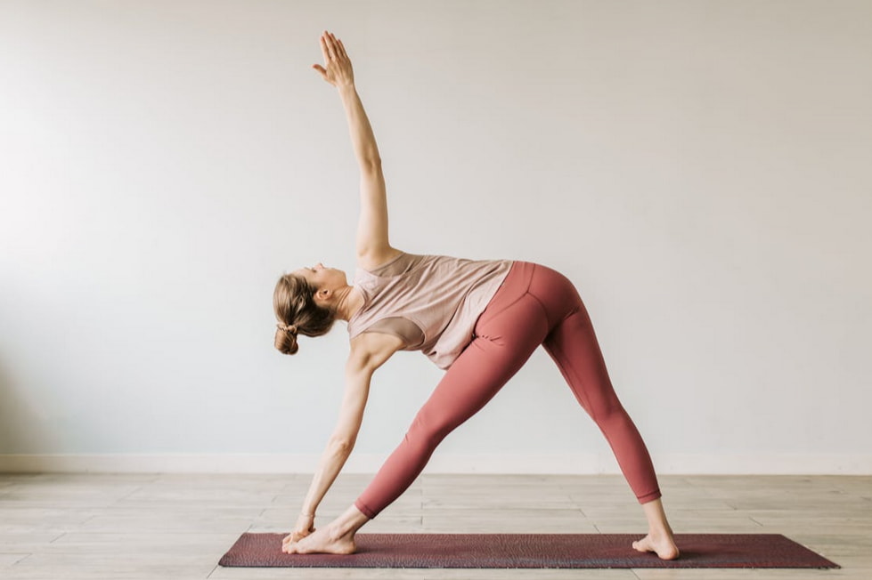 A woman wearing a pink top is engaged in a yoga pose, showcasing her flexibility and concentration.