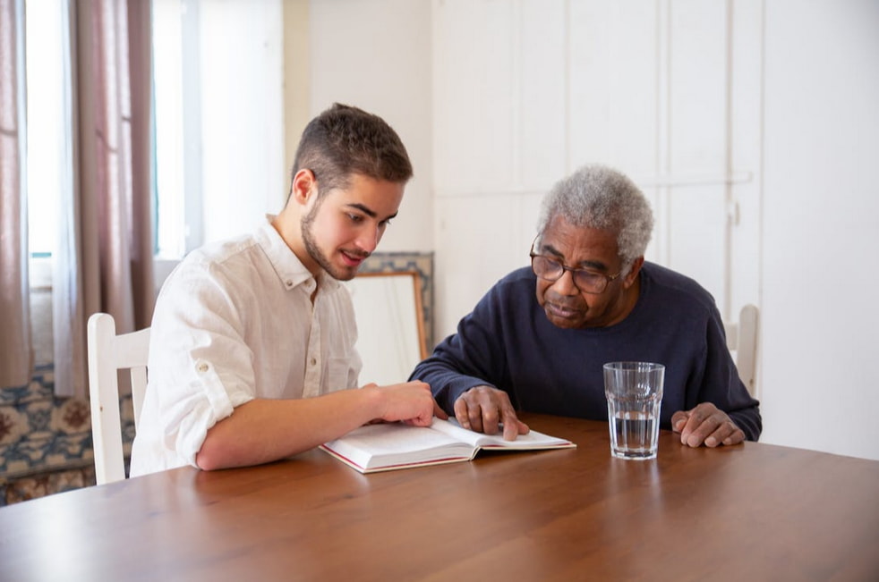 A man and an elderly man are seated at a table, engaged in conversation. 